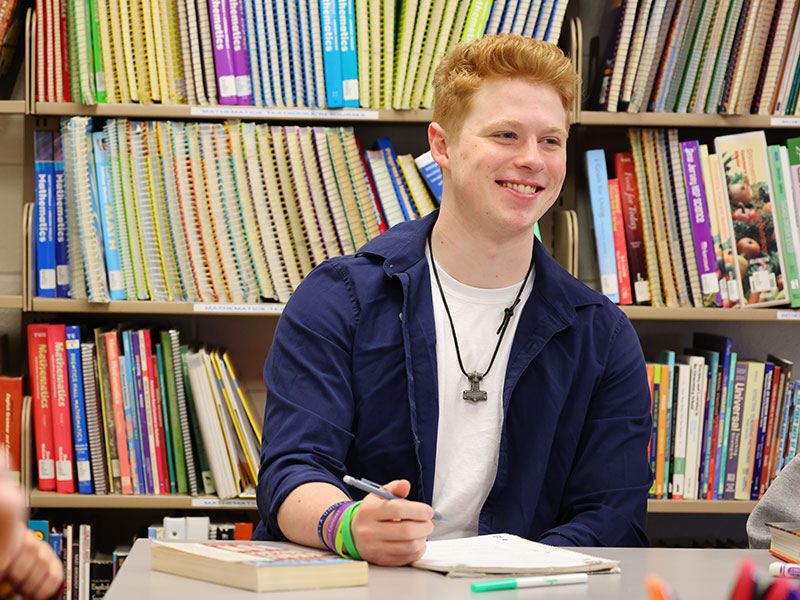 College student working at table, in front of bookshelves