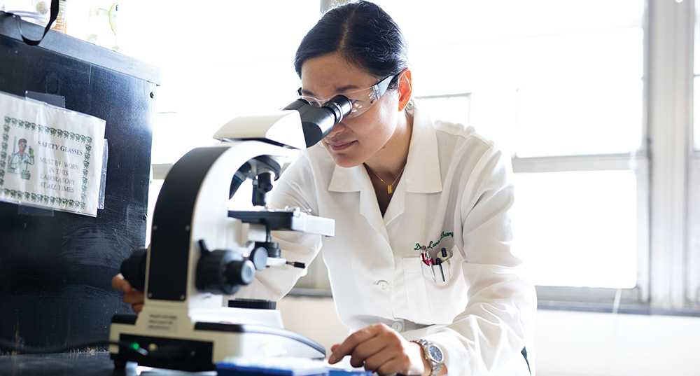 Woman in lab coat looking through a microscope