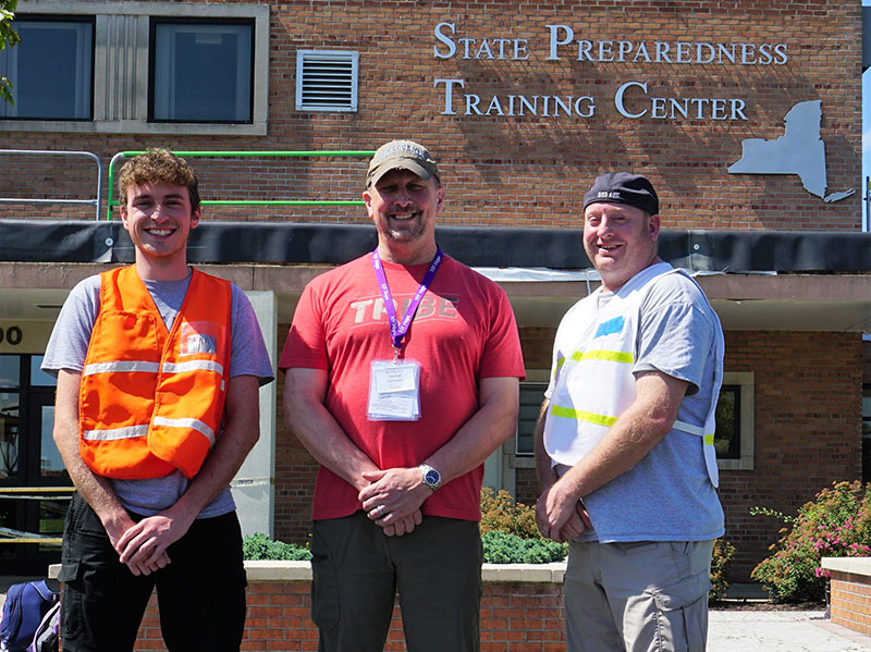 Three men standing in front of building and sign "State Preparedness Training Center"