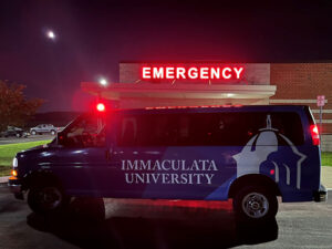 Van with Immaculata University logo on its side, in front of an emergency room.