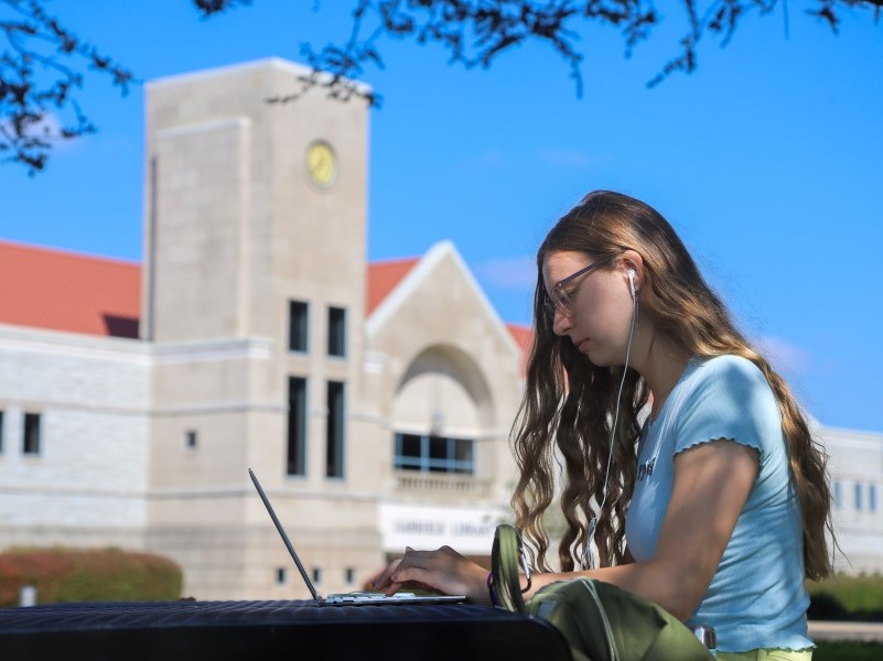 College student sitting outside library, working on laptop computer