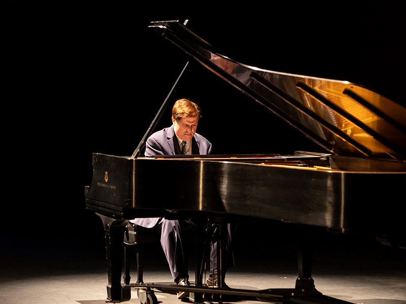 Man in suit on stage playing a piano