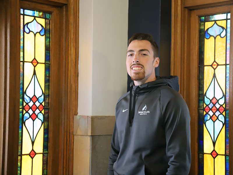 Young man in sweatshirt in front of stained glass windows.
