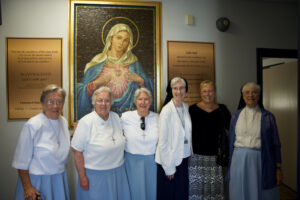 Six nuns standing in front of a painting of Virgin Mary