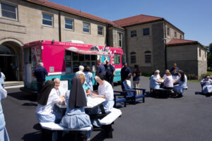 Nuns sitting at tables outside next to an ice cream truck