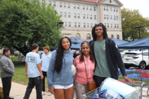 Two women and a man posing while carrying items