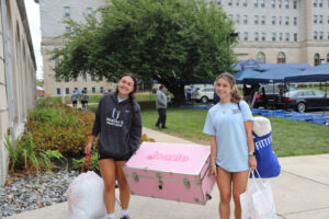 Two young women carrying items to move into dorm