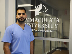 Man in blue scrubs in front of sign that says Immaculata University Division of Nursing