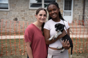 Two young women facing camera while holding a puppy