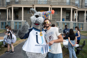 Costumed mascot Mac, a dog, posing with a college student