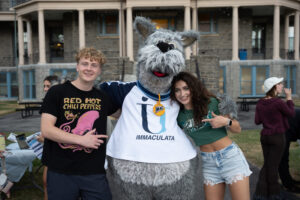 Costumed mascot Mac, a dog, posing with two college students
