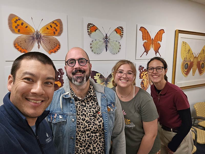 Two men and two young women in front of images of butterflies on a wall