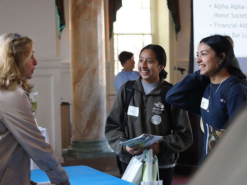 Two young women talking to woman who is standing behind a table