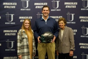 Man holding Eagles football helmet standing between two woemn