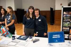 Nun and woman behind table with sign "Campus Ministry"