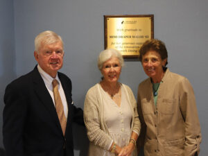 A man and two women in front of plaque dedicating a dining hall