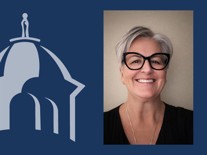 Split image with a navy-blue graphic of a domed building and small human figure on the left, and a professional headshot on the right of a smiling woman with short gray hair, black cat-eye glasses, and a black top against a neutral background.