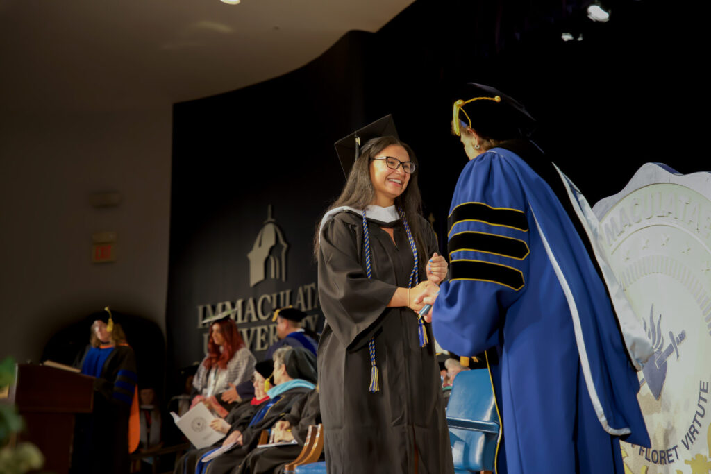 Young graduate shaking university President's hand as she receives her diploma