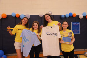 Four women holding up t-shirts that say Mac-a-thon.