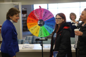 Woman speaks to two people in front of a spinning wheel