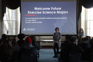 Woman speaking to a group of people in from of a screen that says "welcome future exercise science majors."