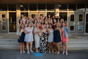 Group of young women posing together on the steps outside a building, smiling and making peace signs.