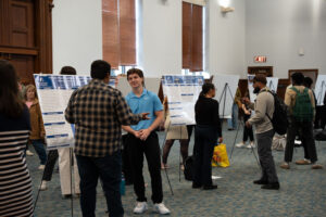 People stand and talk beside research posters on display boards in a large conference hall.