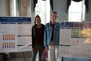 Two students stand beside large research posters on display in a bright hall, presenting their work at a conference.