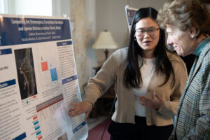 Two women discuss a university poster presentation featuring charts and images on a science research topic.
