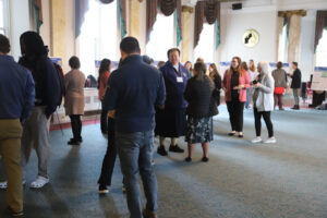 Group of people chatting in a conference hall with poster boards along the walls.