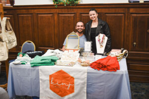 Two people stand behind tbale shwoing clothing