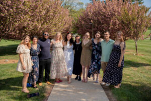 Group of eleven adults posing together on a park path with pink flowering trees behind them on a sunny day Cool spring outdoor photo.