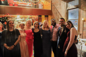 Group of friends in formal attire posing together at a festive party in a decorated room.