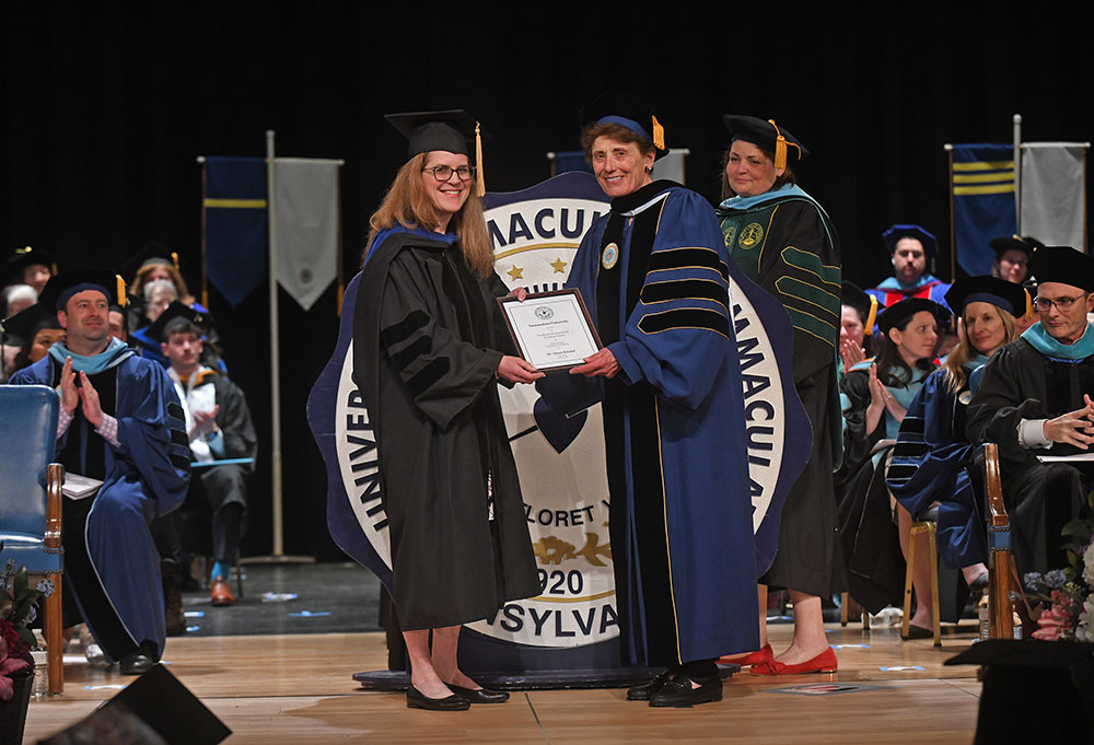 kreibel - Immaculata University Two women on stage in academic robes. One is presenting an award to the other.
