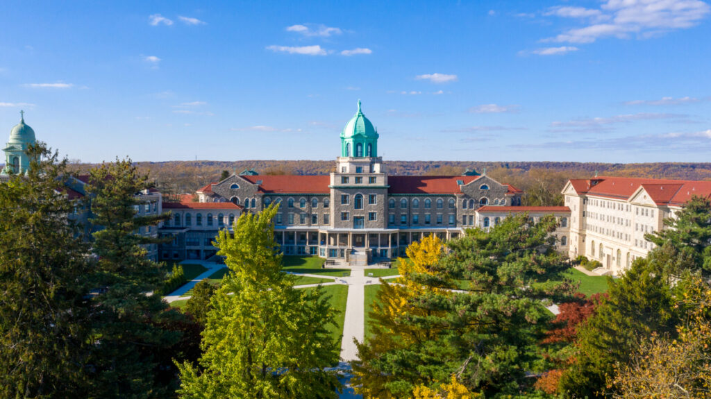 Aerial view of Immaculata University's back campus: central stone building with a green dome, red-roofed wings, and fall foliage.