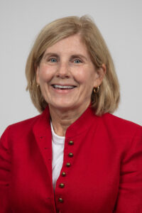 Flite_Cathy - Immaculata University Portrait of a smiling woman with blonde hair wearing a red blazer against a light-gray background.