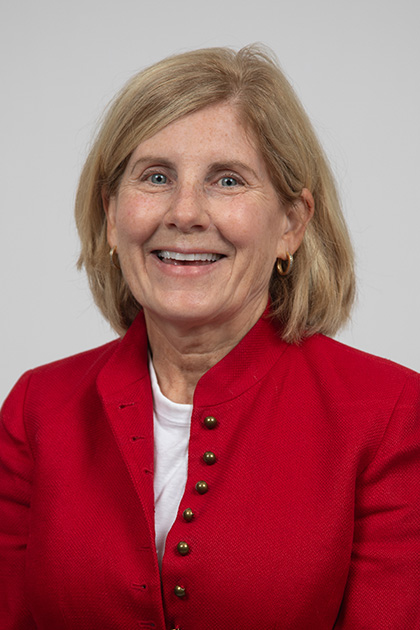 Portrait of a smiling woman with blonde hair wearing a red blazer against a light-gray background.