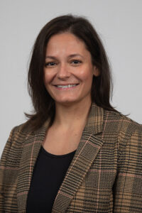 Pressley_Shaney - Immaculata University Smiling woman with shoulder-length brown hair wearing a brown plaid blazer and black top, neutral gray background.