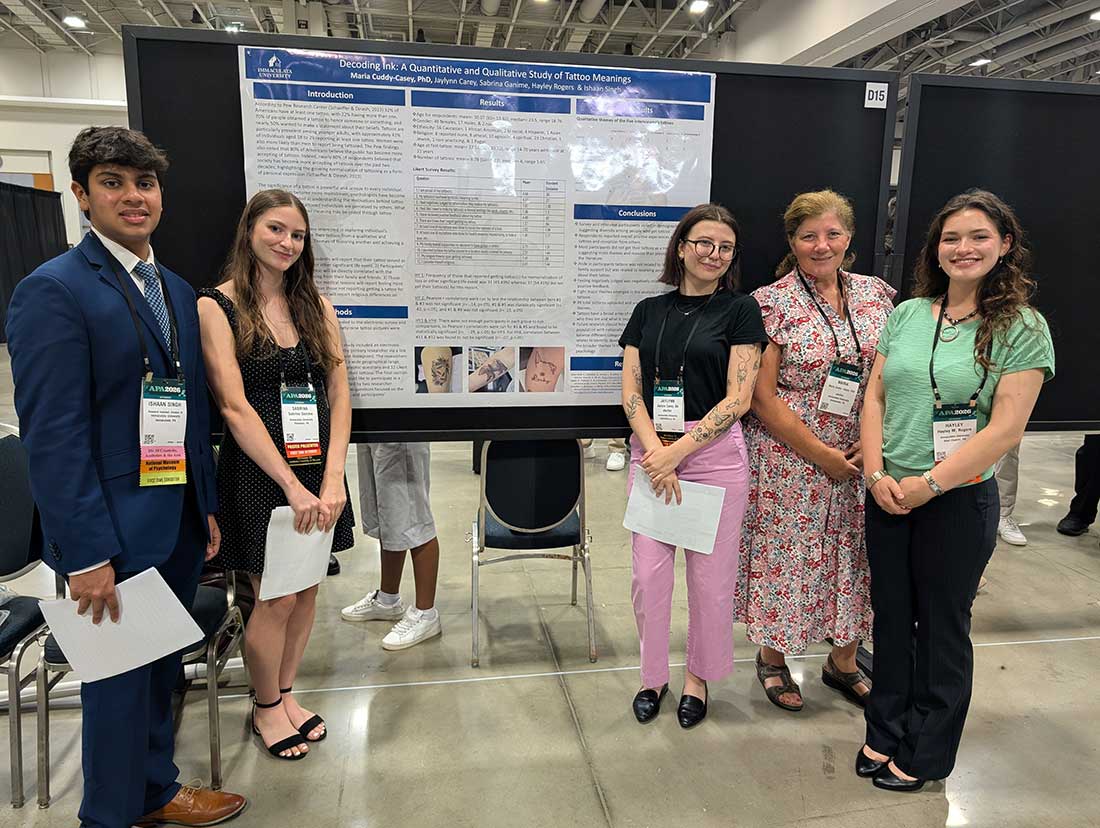 apa-01 - Immaculata University Five researchers posing beside a large research poster at a conference venue, all wearing name badges.