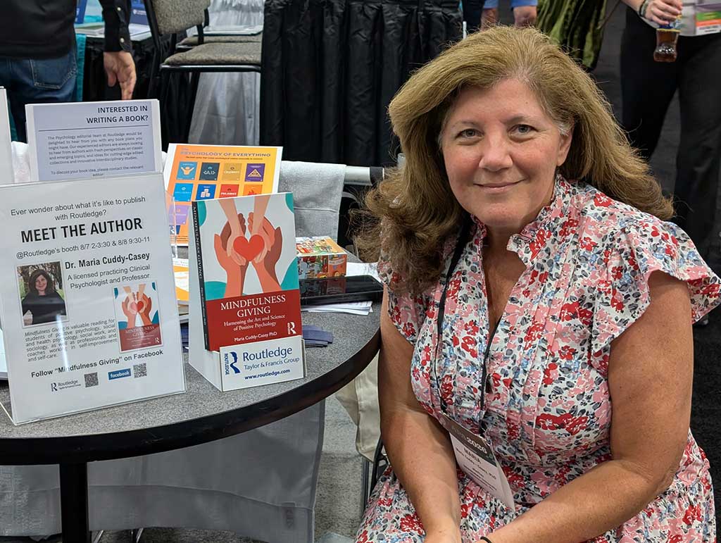 apa-02 - Immaculata University Woman in a floral dress sits at a round booth table with mindfulness books and author posters on display.