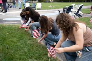 Group of people kneeling on a lawn, placing small American flags along a path at a park event.