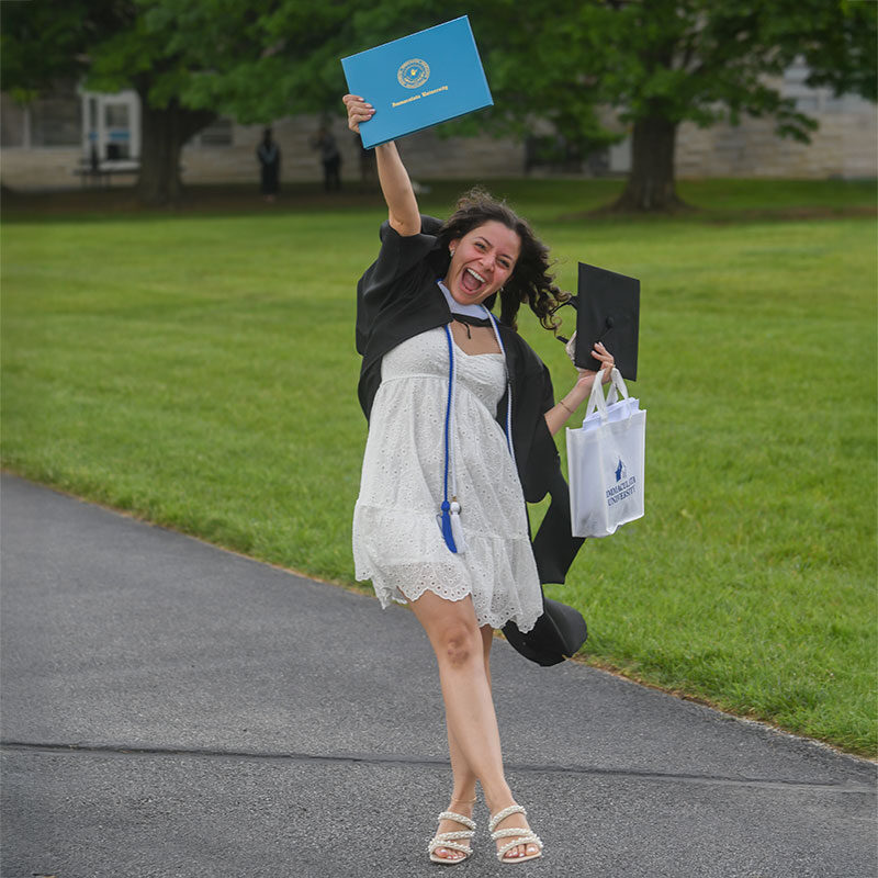 Young woman in cap and gown holding up her diploma