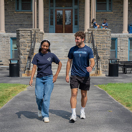 A young woman and young man walking in front of an old college building